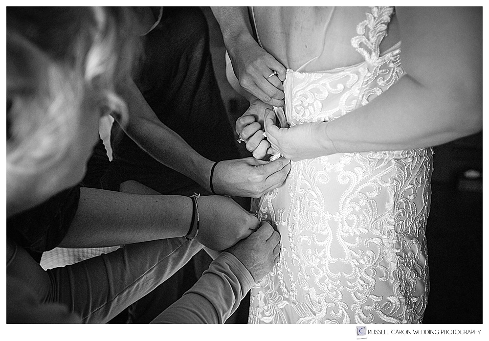 black and white photo of bride getting her dress fastened by many hands
