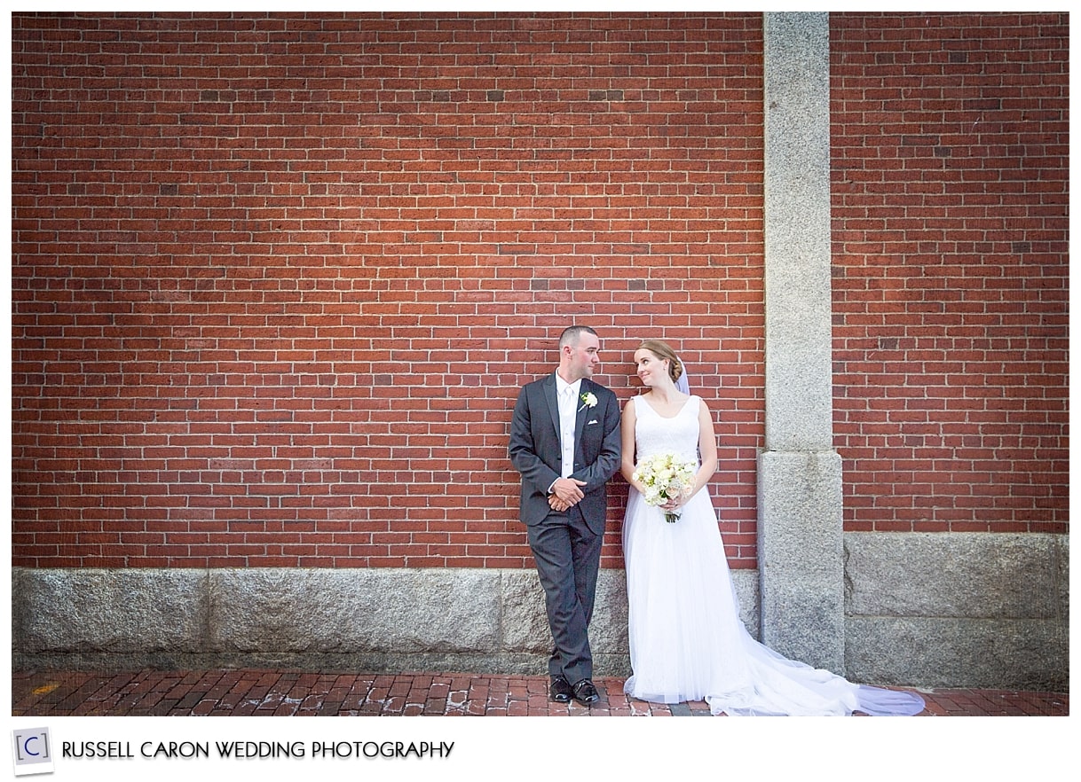 Bride and groom in front of brick wall in Portland Maine, by Portland Maine wedding photographers, Russell Caron Wedding Photography