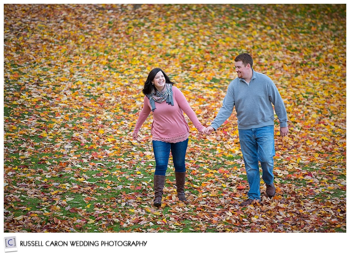 Couple holding hands, walking through autumn leaves