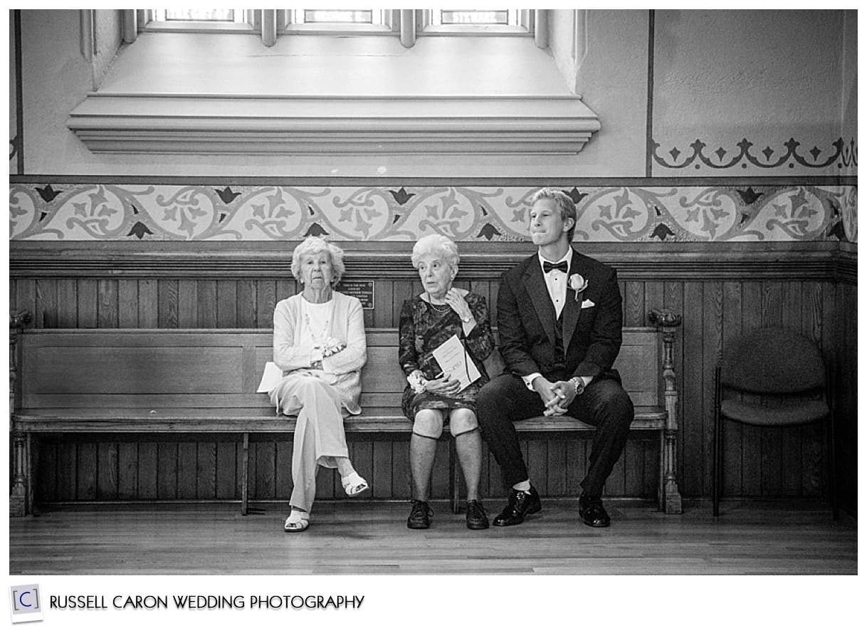 Best man and grandmothers sitting on bench at back of the church