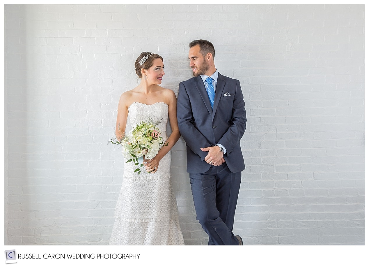 Bride and groom against white brick wall in lighthouse
