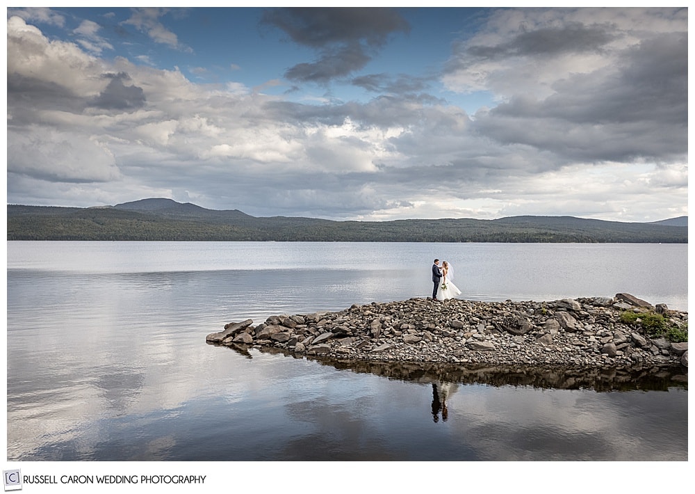 breathtaking scenic wedding portrait of a bride and groom standing on a spit of land in a New Hampshire Lake