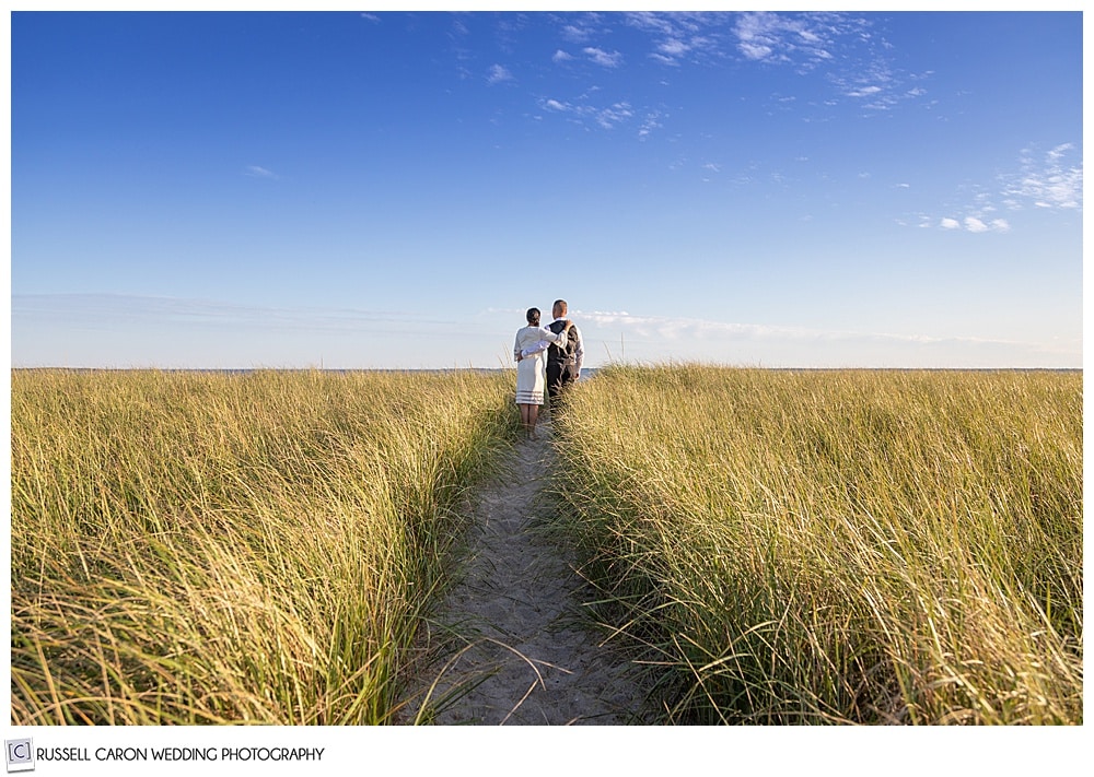 seaside elopement photo of a bride and groom walking through the sand dunes at Pine Point Beach, Scarborough, Maine