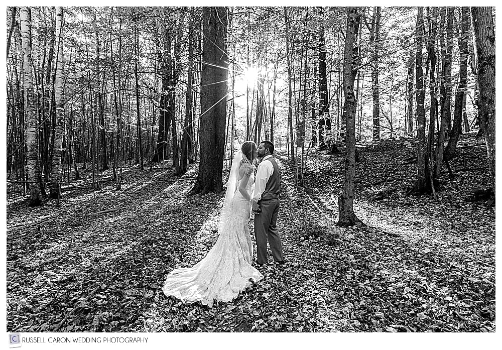 black and white photo of bride and groom kissing in the woods