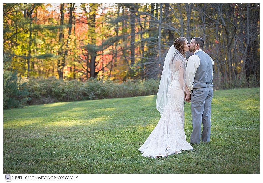 bride and groom kissing each other on a hill with fall foliage