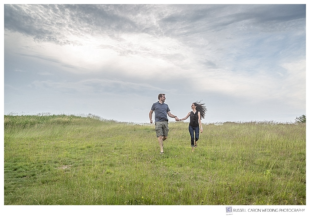 Man and woman holding hands, walking down a grassy hill. 2017 Favorite Maine engagement images 