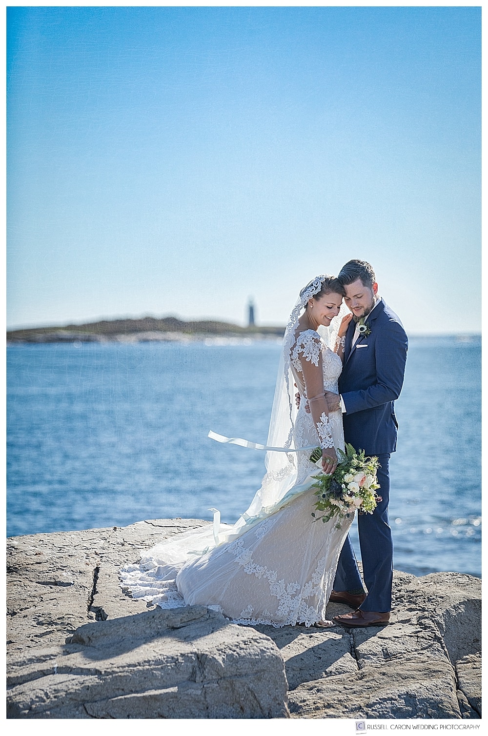 Bride and groom with their foreheads together with a lighthouse behind them