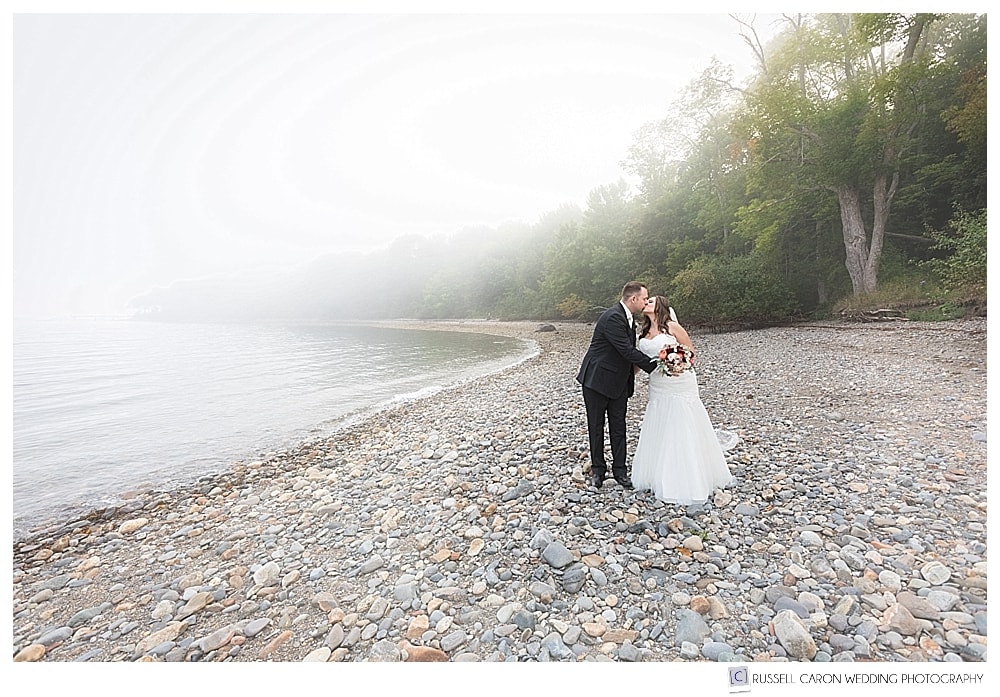 Bride and groom kissing on a foggy Maine beach. 