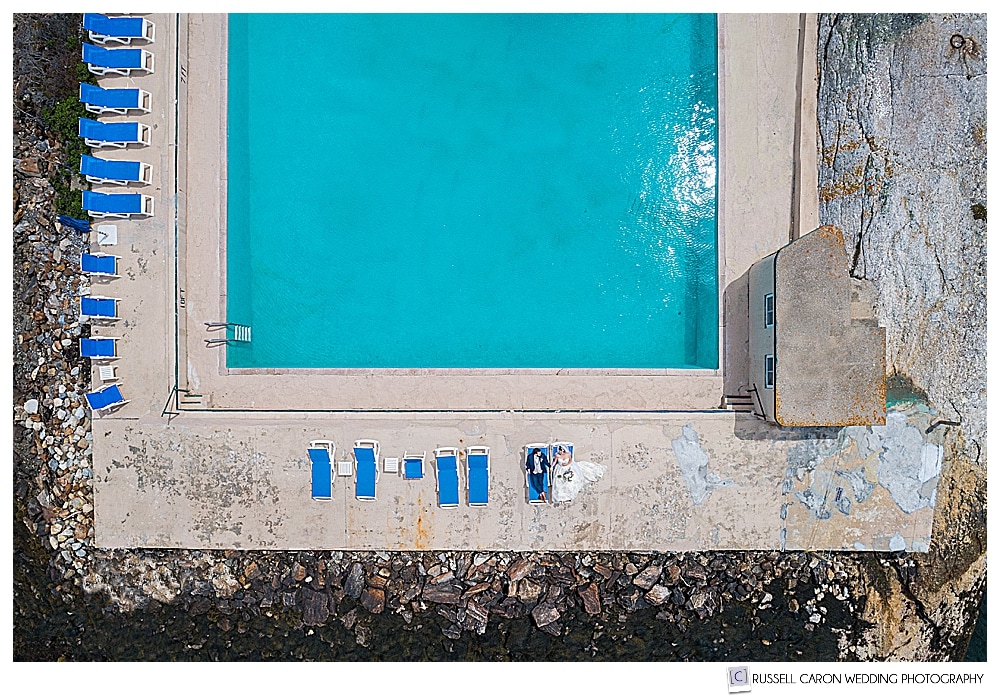 Beautiful Maine drone wedding photo of a bride and groom sitting at the salt water pool at their Sebasco Harbor Resort wedding, Phippsburg, Maine