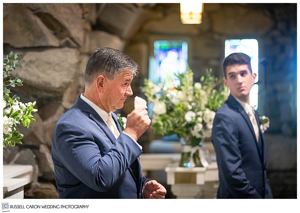 a groom, standing before the altar at St. Ann's Episcopal Church, Kennebunkport, Maine, hie's dabbing at his eyes with a handkerchief, his son is turning to look at him