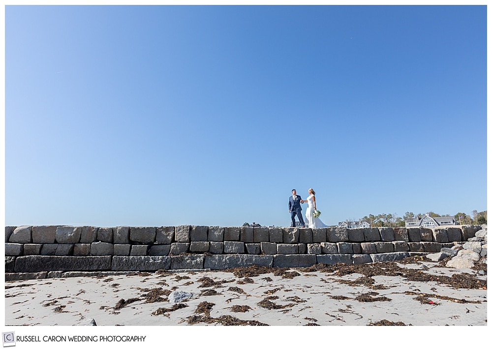 bride and groom walking together on the kennebunkport, maine, breakwater