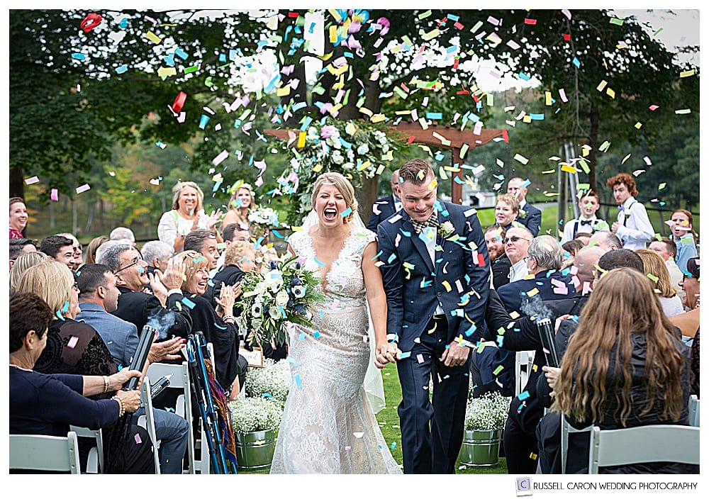 Bride and groom during ecstatic wedding recessional with confetti cannons shooting confetti