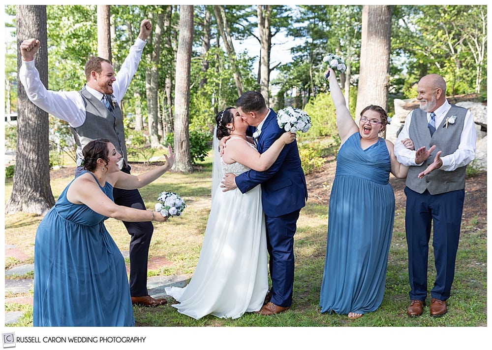 bride and groom kissing while wedding party cheers