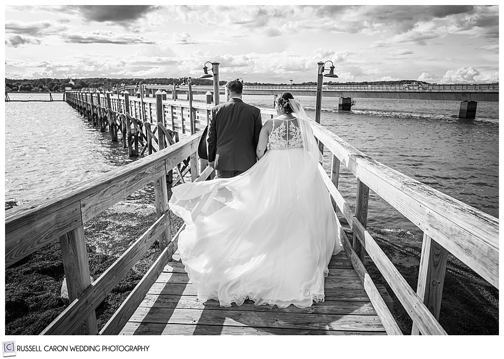 black and white photo of a bride and groom walking on a long dock