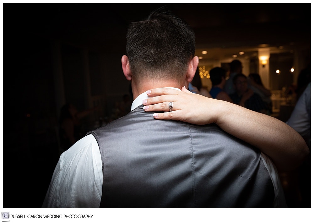 photo of the back of a man, with a woman's hand with wedding rings, on the back of his neck