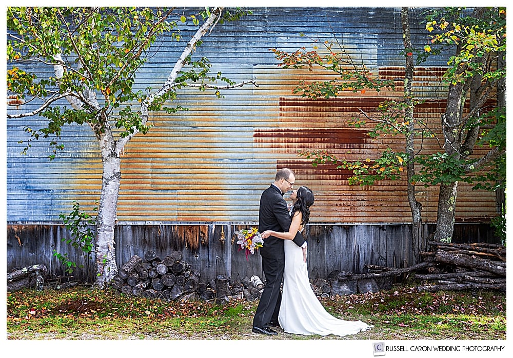 a bride and groom in an environmental wedding photo in front of a weathered barn