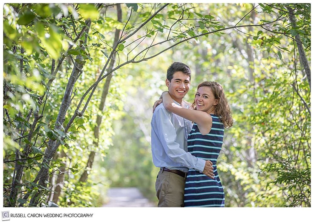 man and woman, in the woods, with their arms around each other, they're looking at the camera