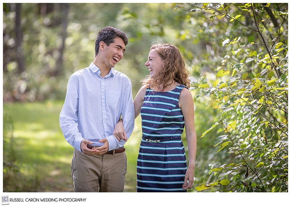 man and woman, in the woods, their arms are linked, and they're laughing at each other