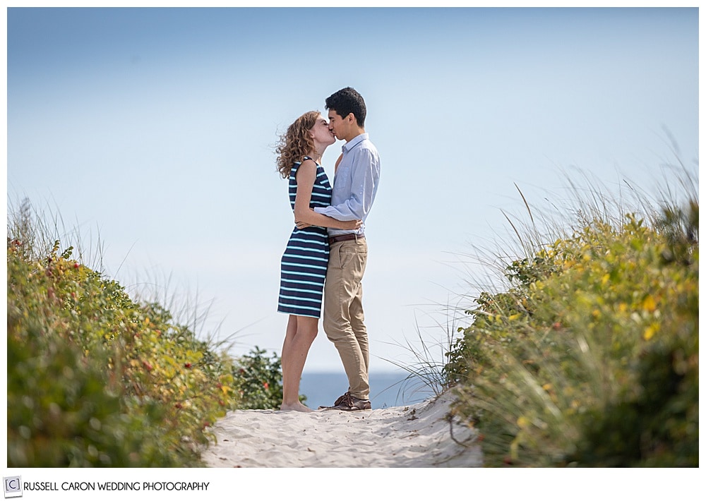 man and woman, standing face to face in the beach dunes, on a path, kissing each other