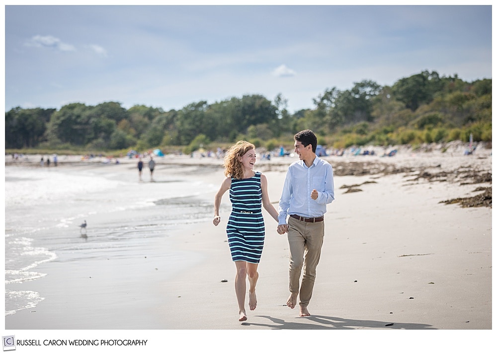 man and woman holding hands and running, they're looking at each other, during their fun crescent beach engagement