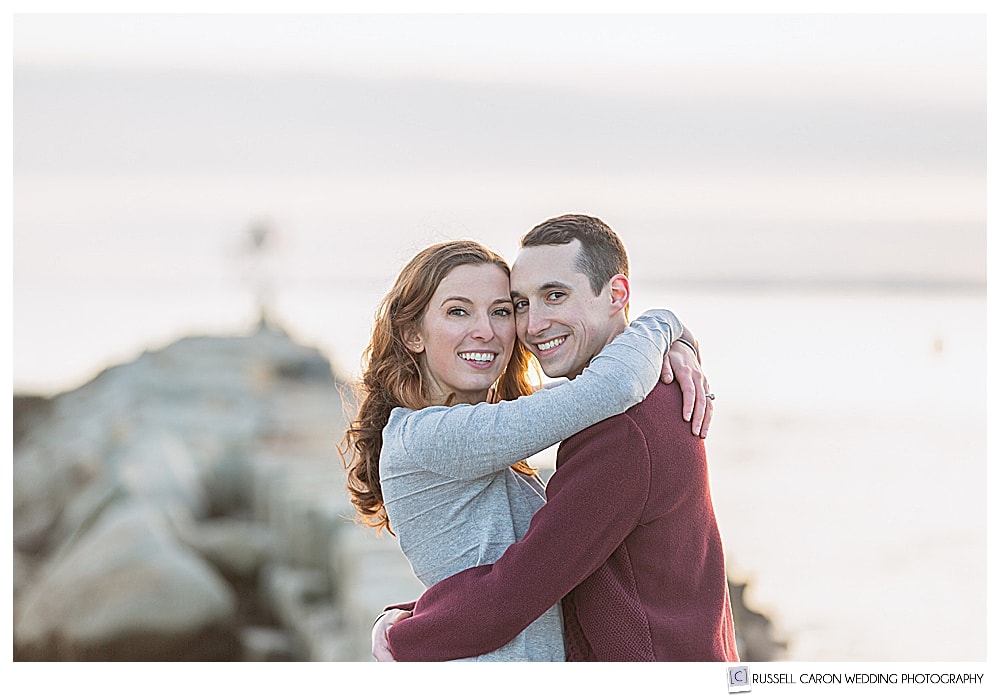 Woman and man hugging, looking at the camera during their Kennebunkport engagement photo session