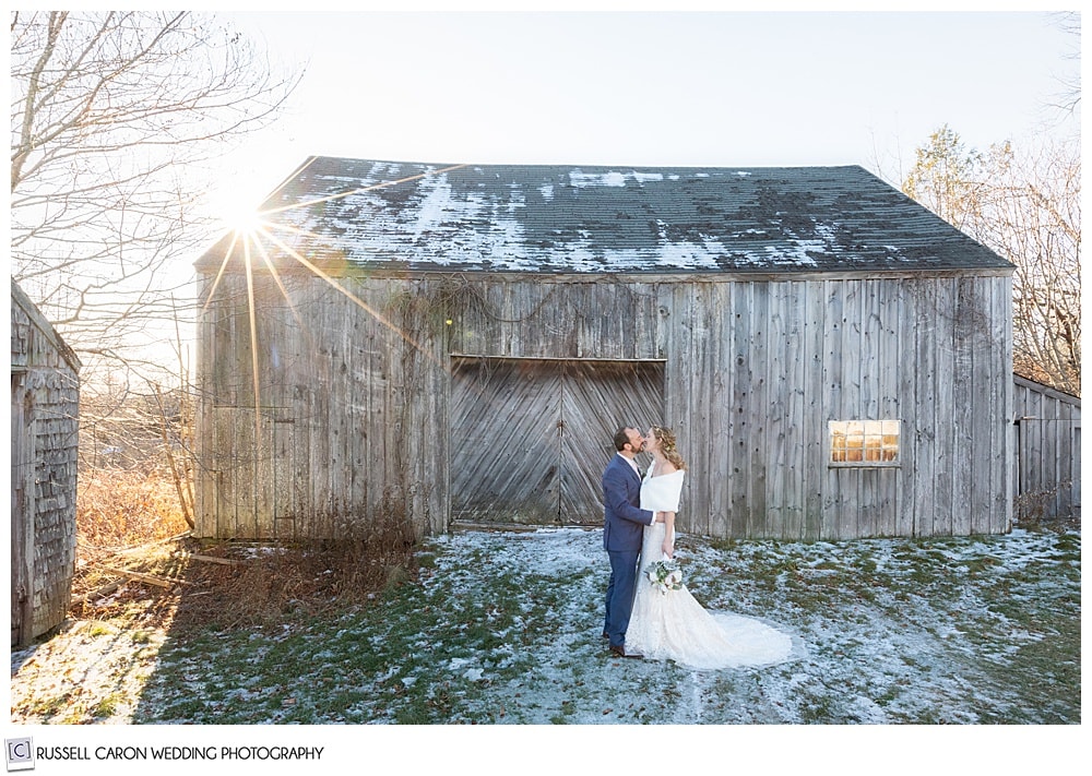 bride and groom kissing in front of an old barn