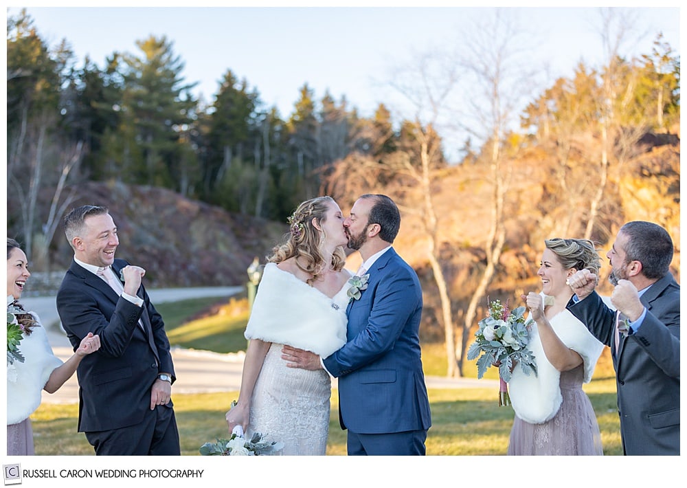 bride and groom kissing while their bridal party cheers