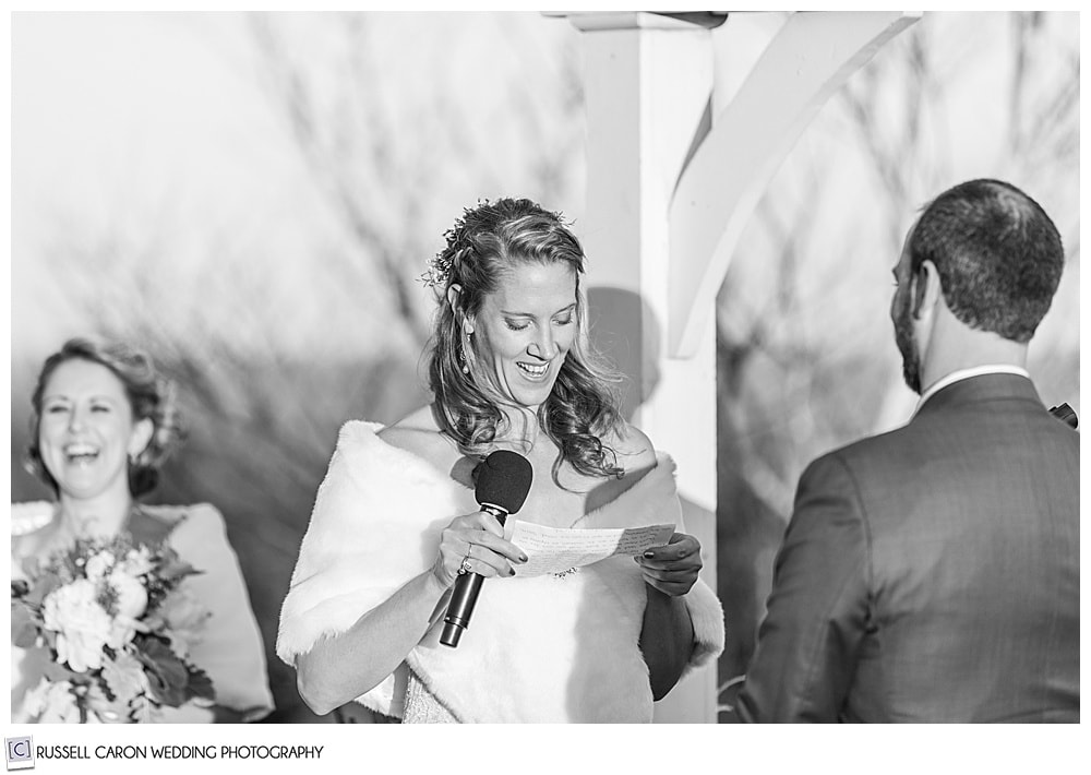 black and white photo of bride holding a microphone as she recites her vows during her outdoor midcoast maine wedding ceremony