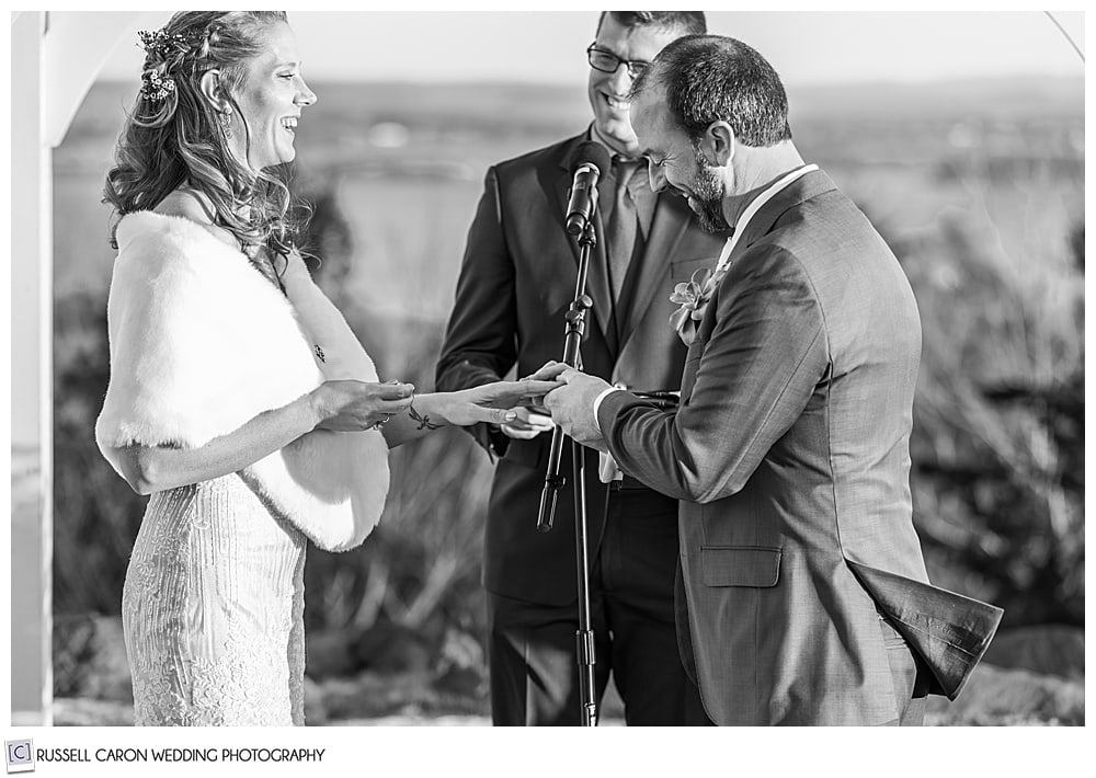 black and white photo of a groom putting the wedding band on his bride's finger during their midcoast maine wedding ceremony at Northport maine