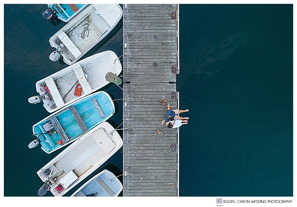 Man and woman sitting on a dock in a Maine drone engagement image on the docks in the York River, Maine