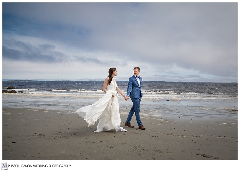 bride and groom walking hand-in-hand on the beach with dark skies