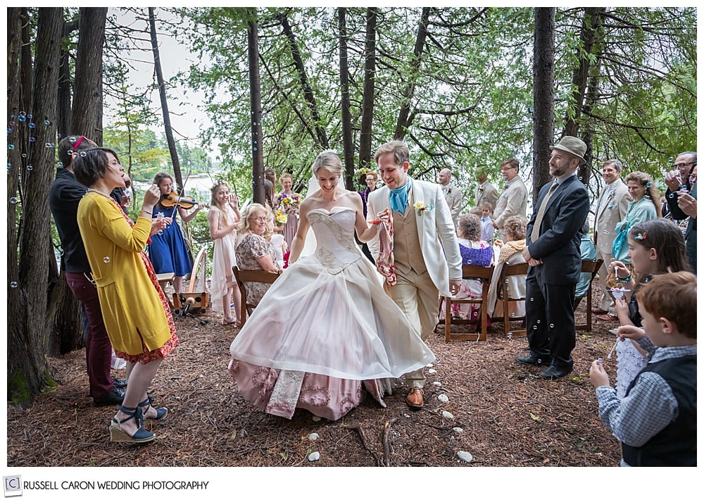 bride and groom, holding hand during their recessional in the woods, while guests blow bubbles