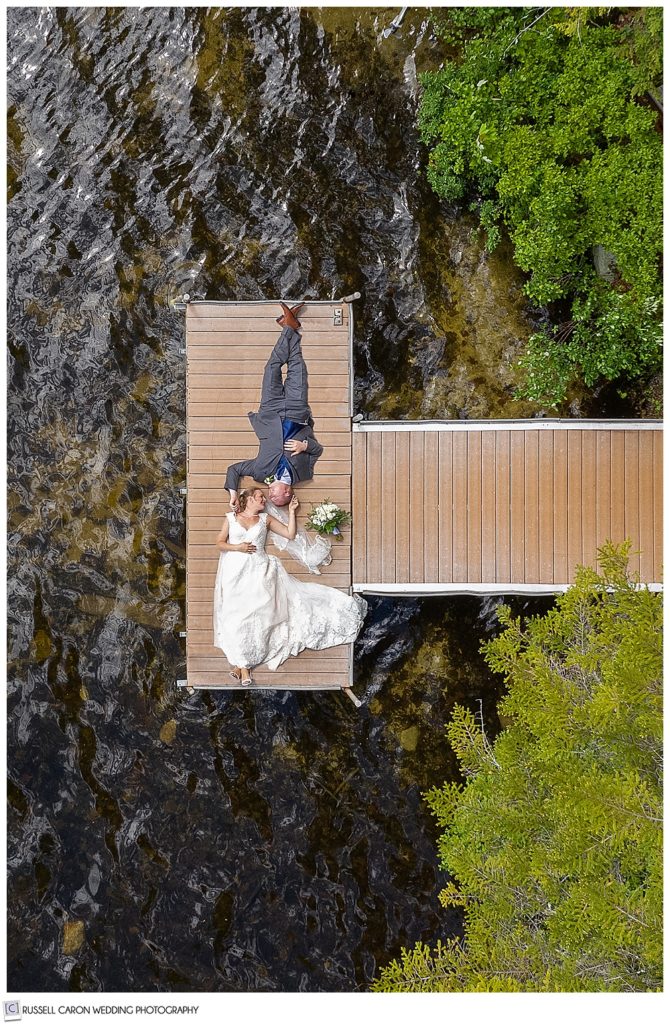 maine wedding photography team captures a maine drone wedding photo of a bride and groom laying on a dock