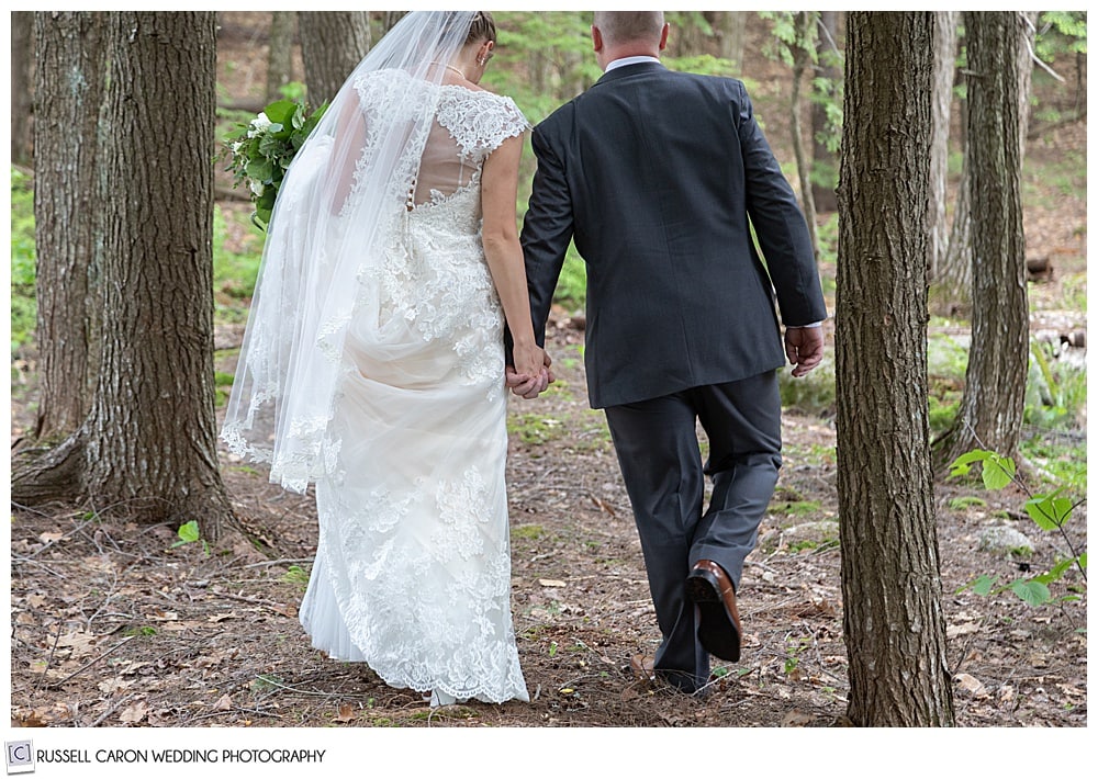 bride and groom holding hands, walking away in the woods