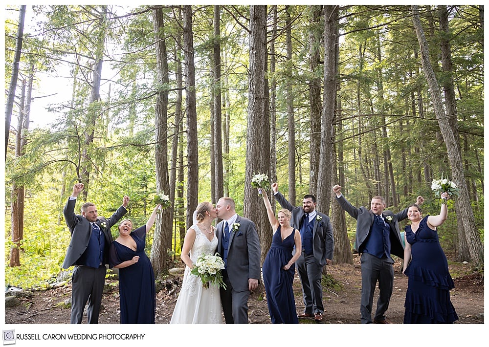 photo of bridal party in the woods, bride and groom kissing, everyone cheering