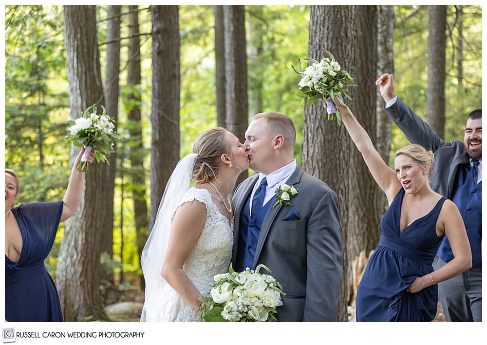 bride and groom in the woods, kissing, while bridal party cheer