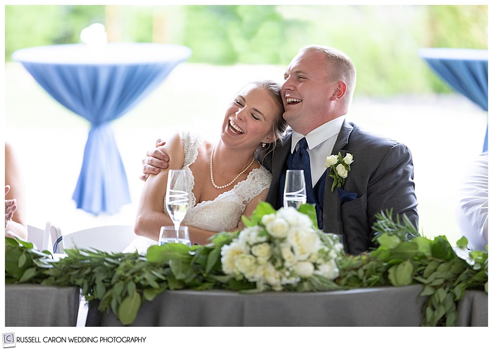 groom hugging bride as she sits next to him, both are laughing