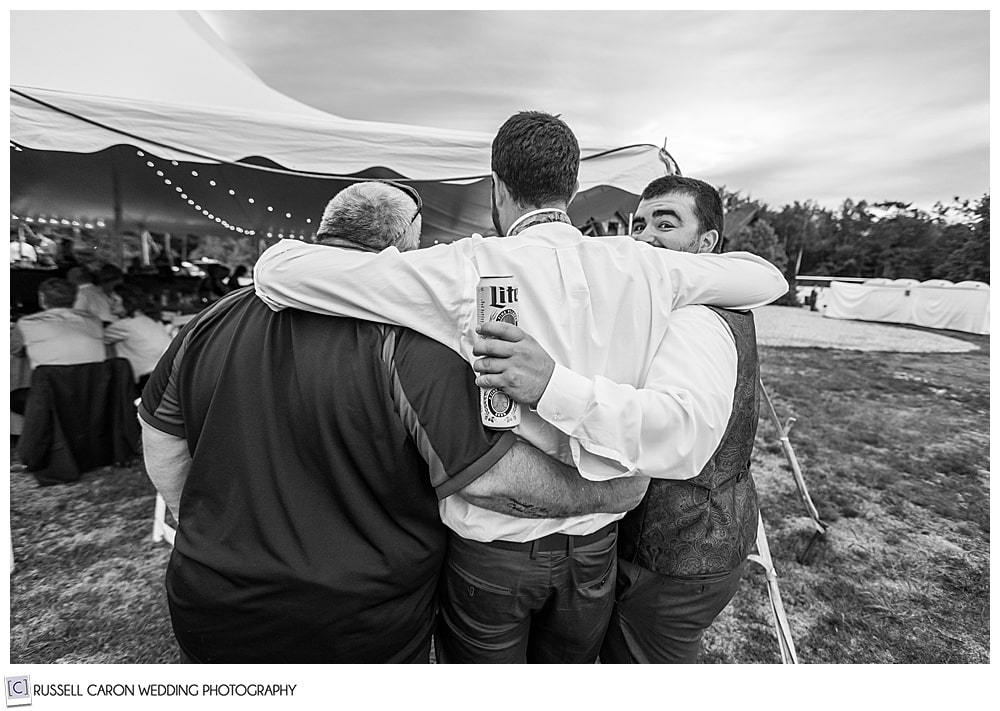 black and white photo of three guys hugging , their backs are to the camera