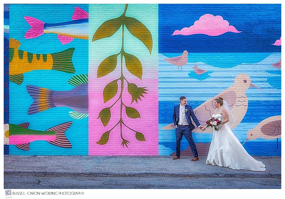 bride and groom walking by the Grasshopper Shop mural wall in Rockland, Maine