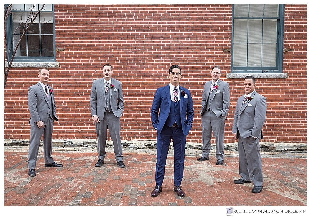 groom and groomsmen in front of brick wall