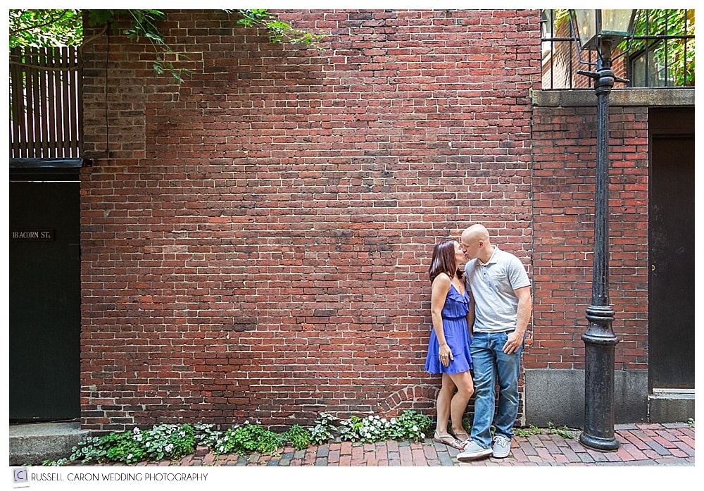 man and woman kissing each other in front of a brick wall during Acorn Street Boston engagement session