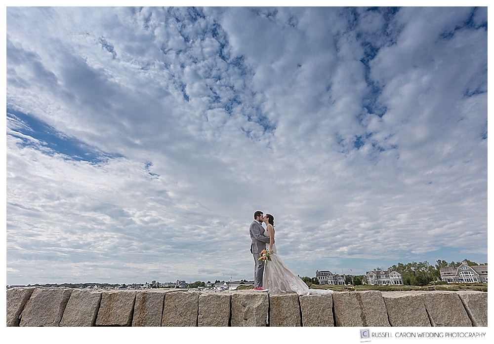 bride and groom standing together on the Kennebunkport Breakwater, with lots of clouds