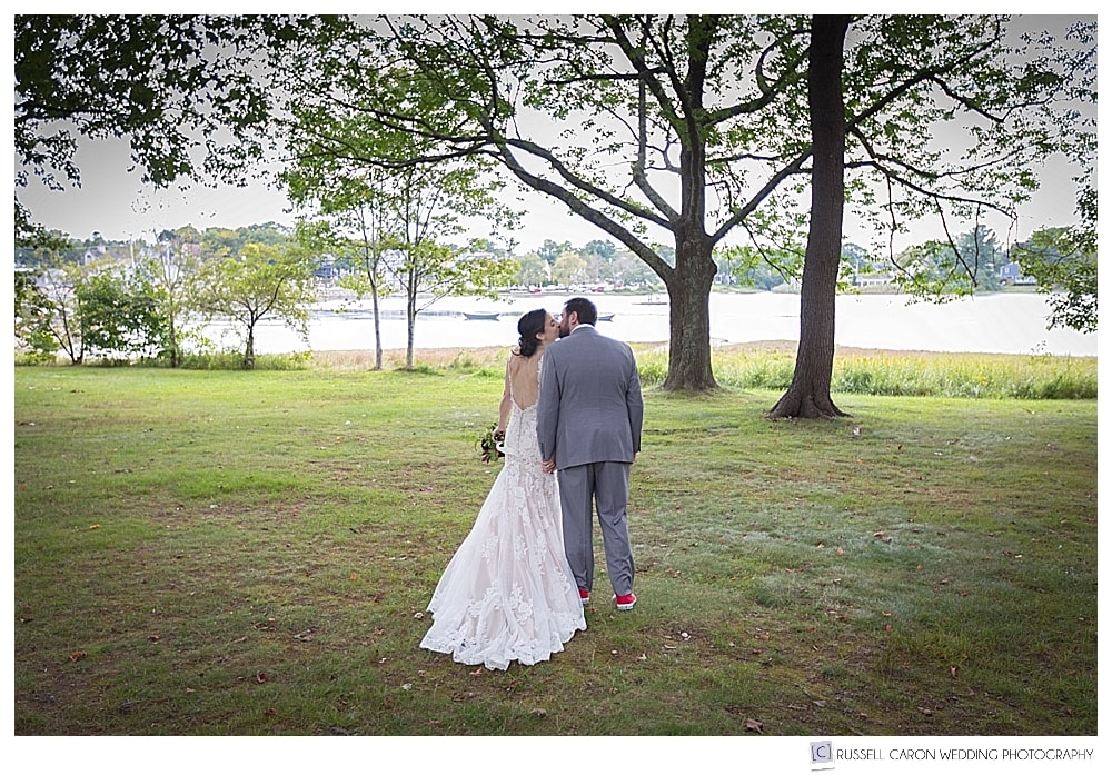 Bride and groom walking and kissing on the banks of the Kennebunk River in Kennebunkport, Maine