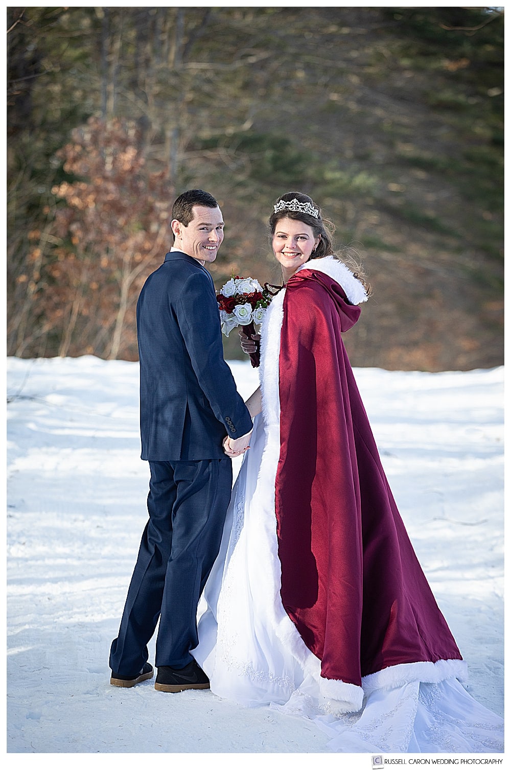 bride with red cape, and groom turn to look at camera during a snowy winter Bethel Maine wedding