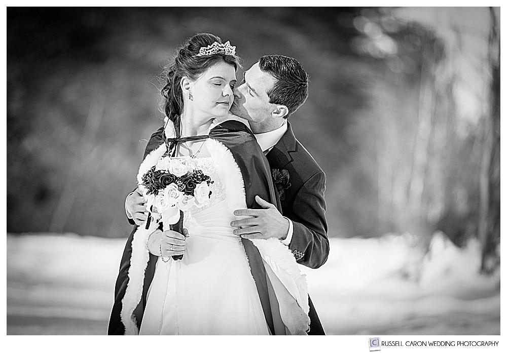 black and white photo of groom kissing bride on her cheek