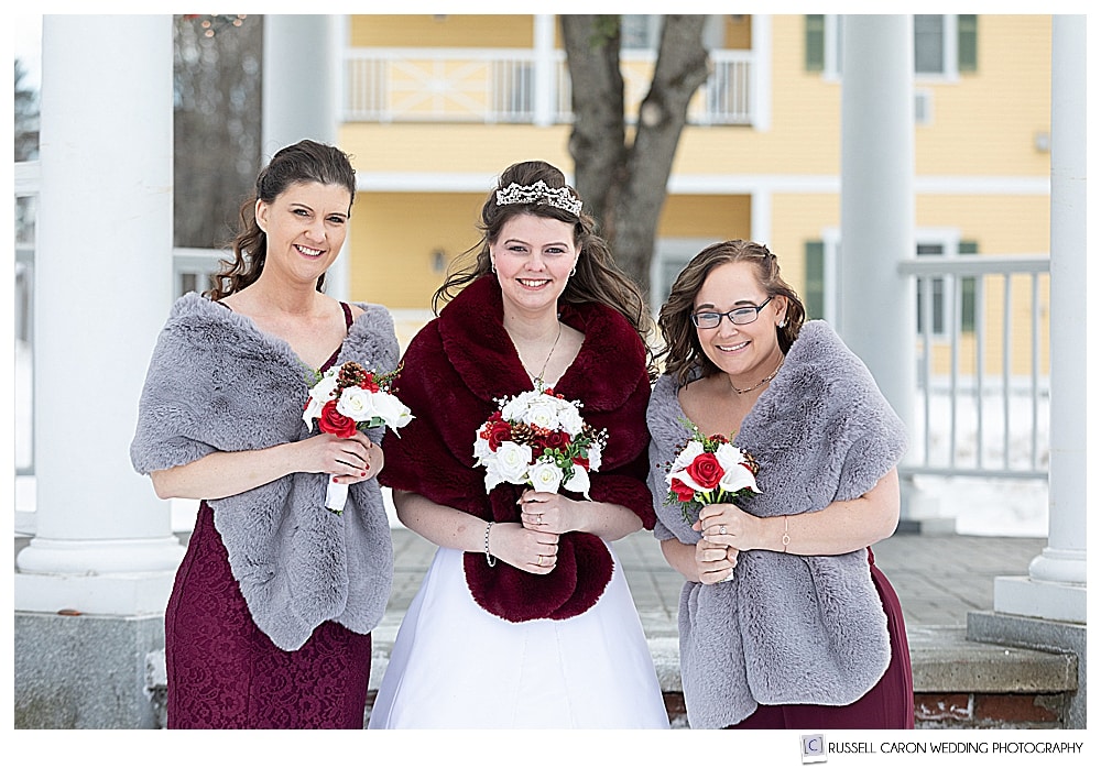 bride and bridesmaids wearing winter stoles in front of the Bethel Inn gazebo during a Maine winter wedding