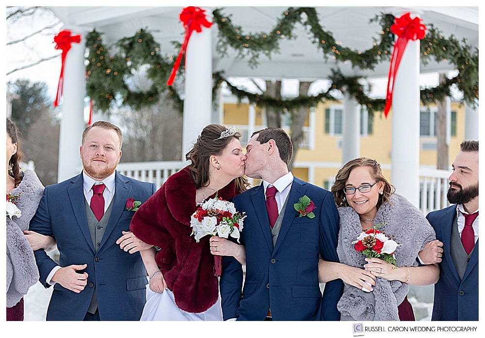 bride and groom kissing with their wedding party in front of the Bethel Maine gazebo