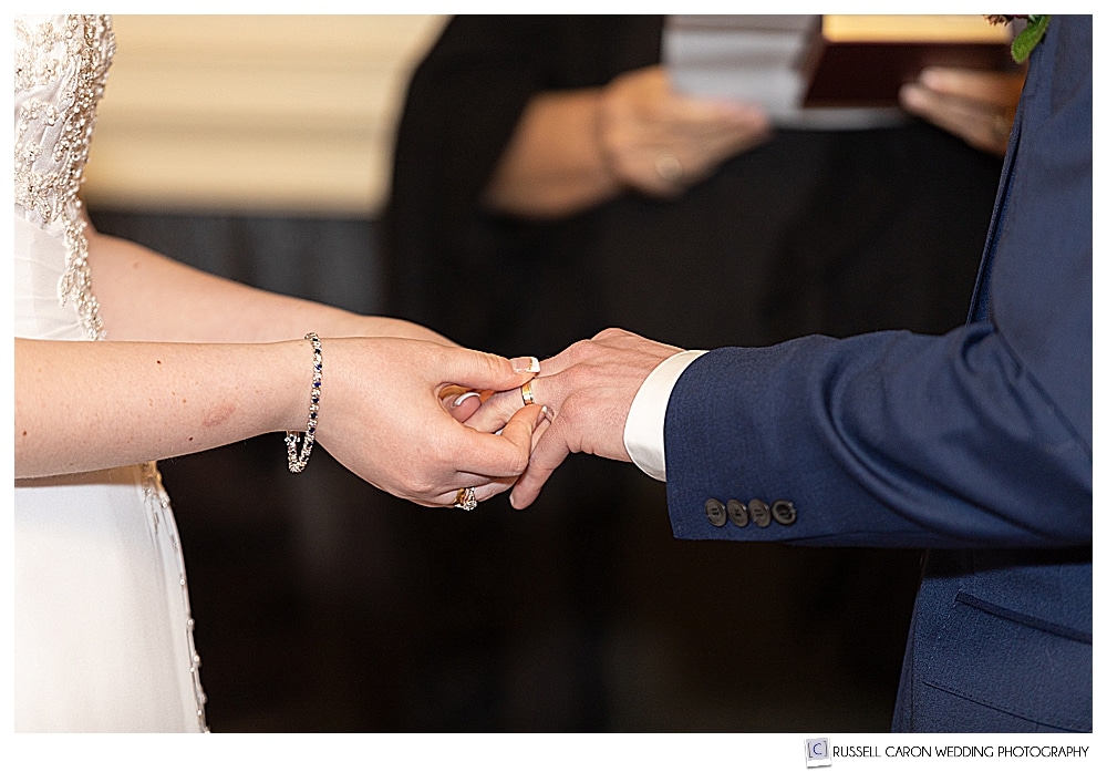 bride puts wedding band on groom's finger during wedding ceremony