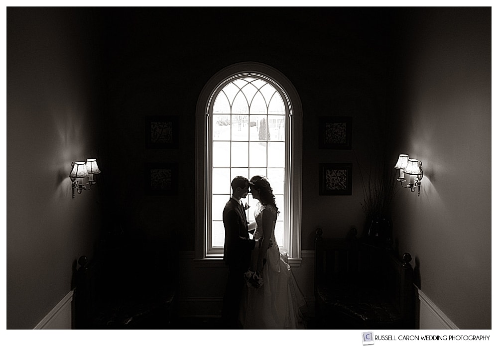black and white photo of bride and groom in front of arched window