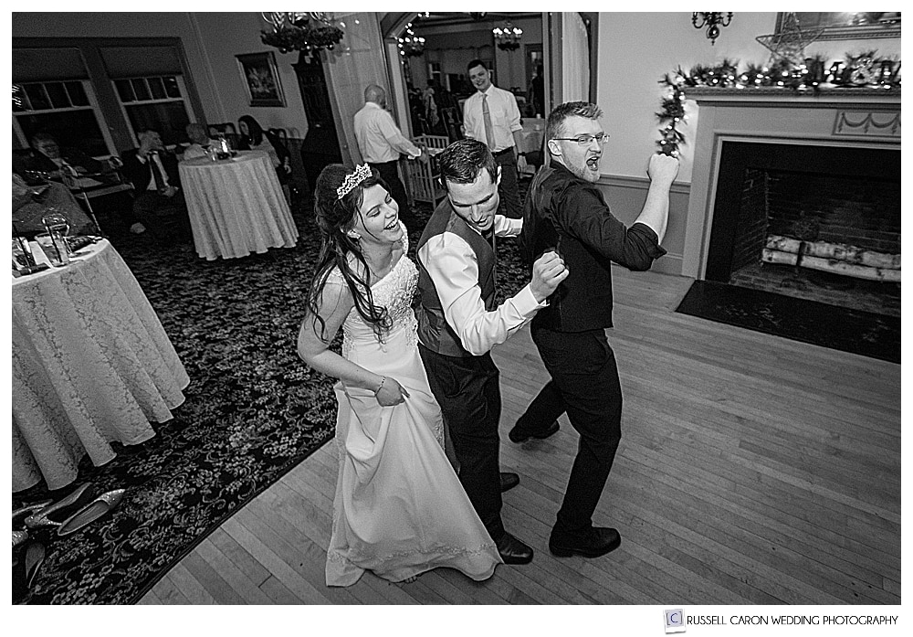 black and white photo of bride, groom, and friend dancing